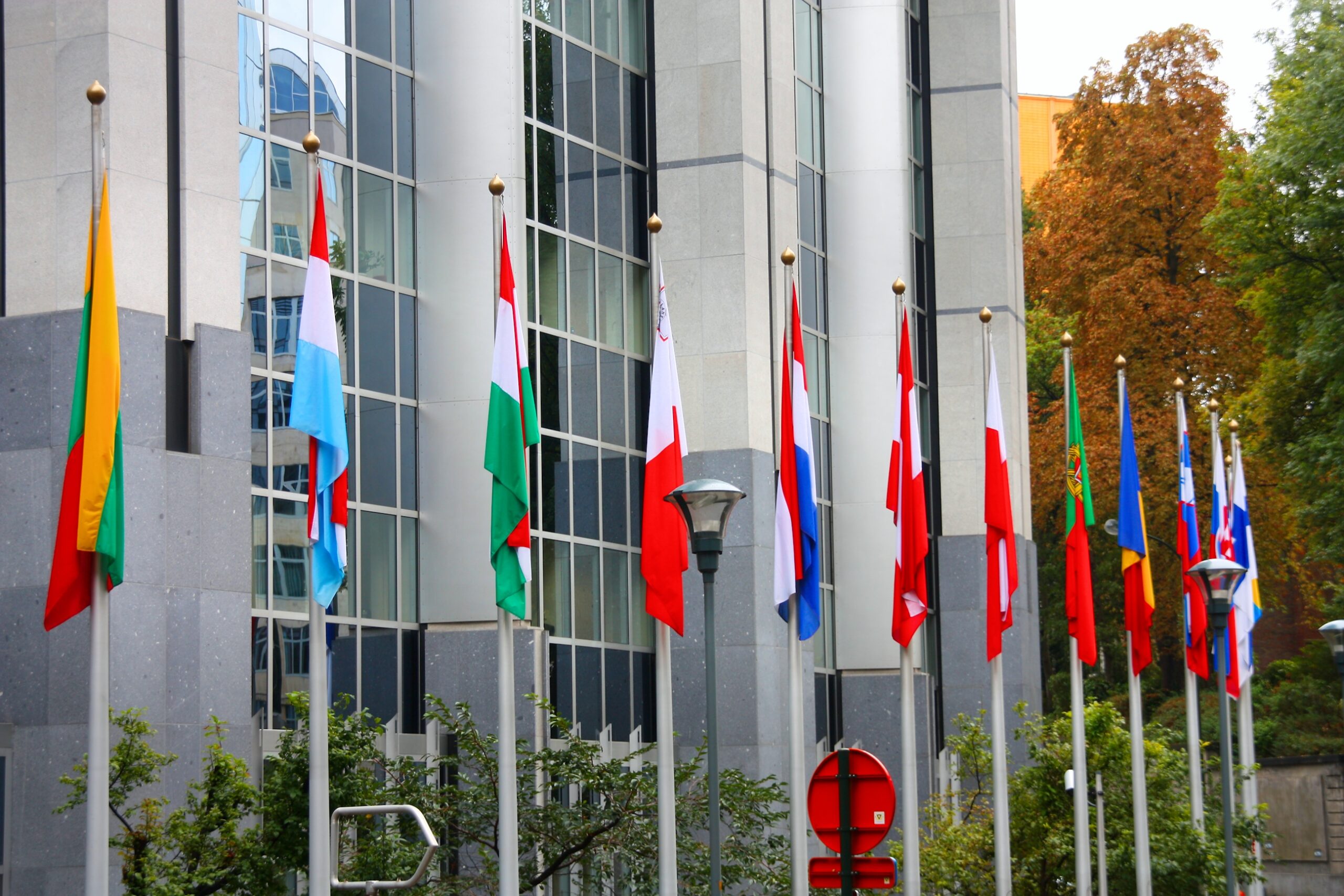 A row of EU member-state national flags on tall flagpoles in front of the Paul-Henri Spaak building of the European Parliament in Brussels.